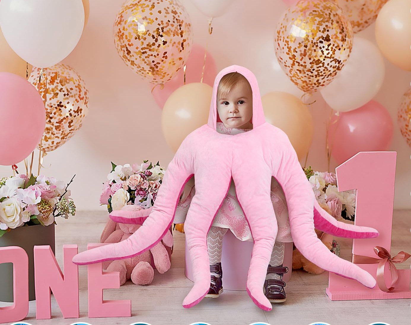 Toddler in the pink octopus costume surrounded by birthday balloons and a number one