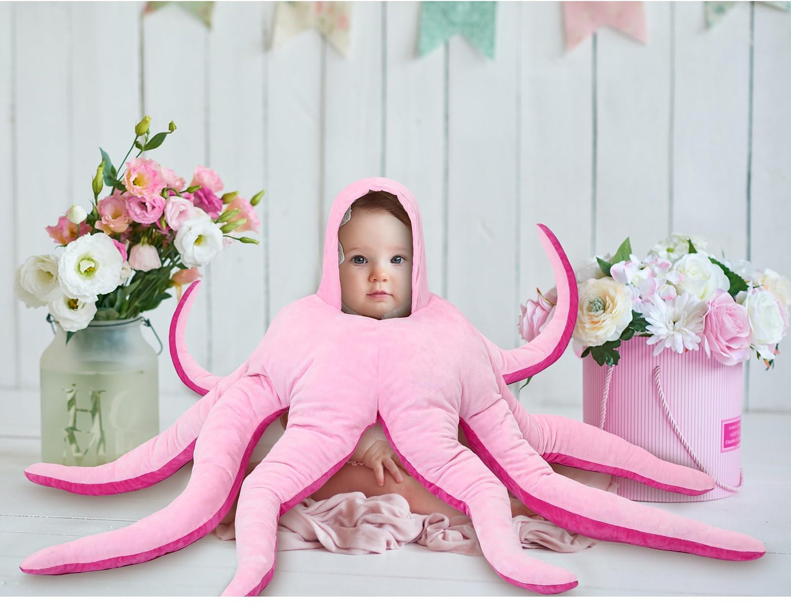 Baby wearing the pink plush octopus costume, tentacles spread across a white wooden floor
